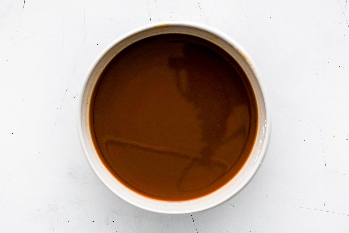 A white bowl filled with smooth brown pineapple chicken sauce mixture.