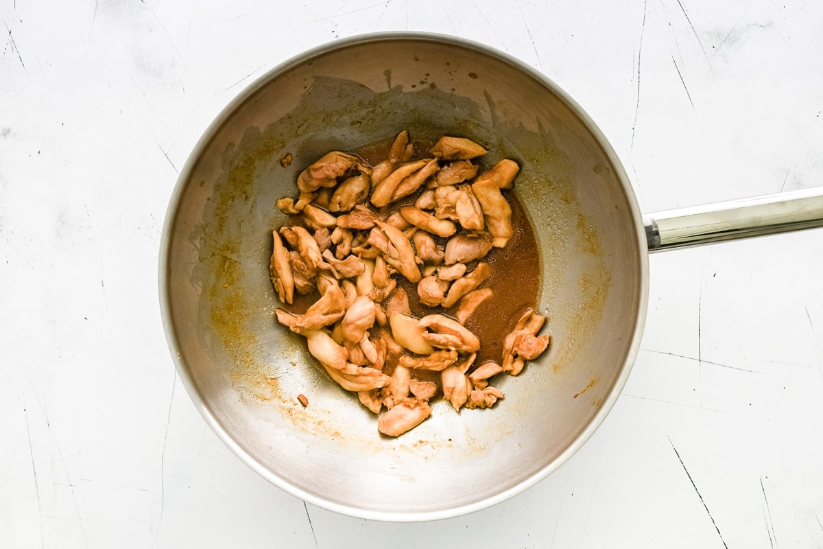 Cooked chicken strips in a stainless steel wok after being stir-fried.