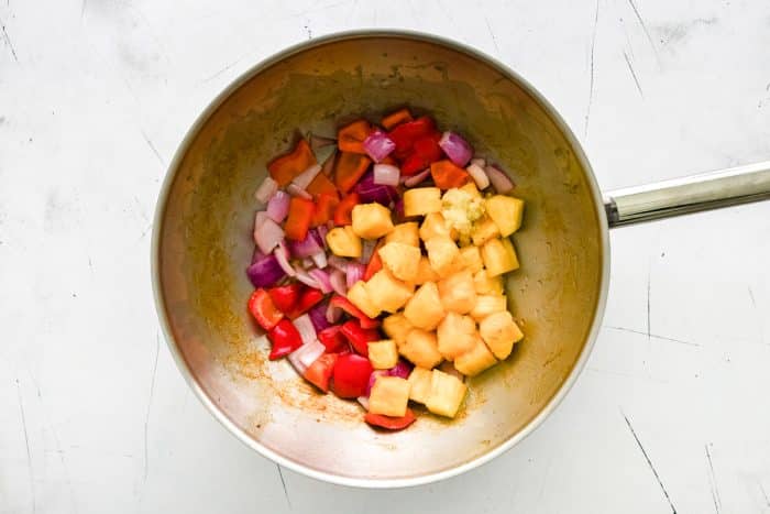 Fresh pineapple chunks, garlic, red onion, and red bell pepper cooking in a stainless steel wok.