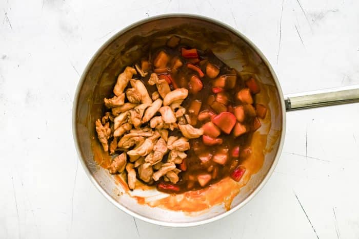Cooked chicken pieces added back into a wok with vegetables and sauce.