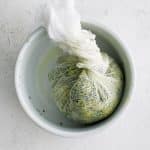Shredded zucchini twisted in a large cheesecloth and placed in a large with bowl.