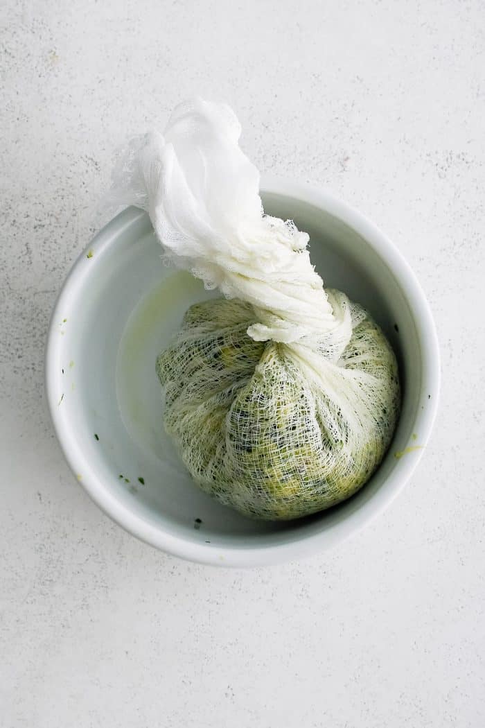 Shredded zucchini twisted in a large cheesecloth and placed in a large with bowl.