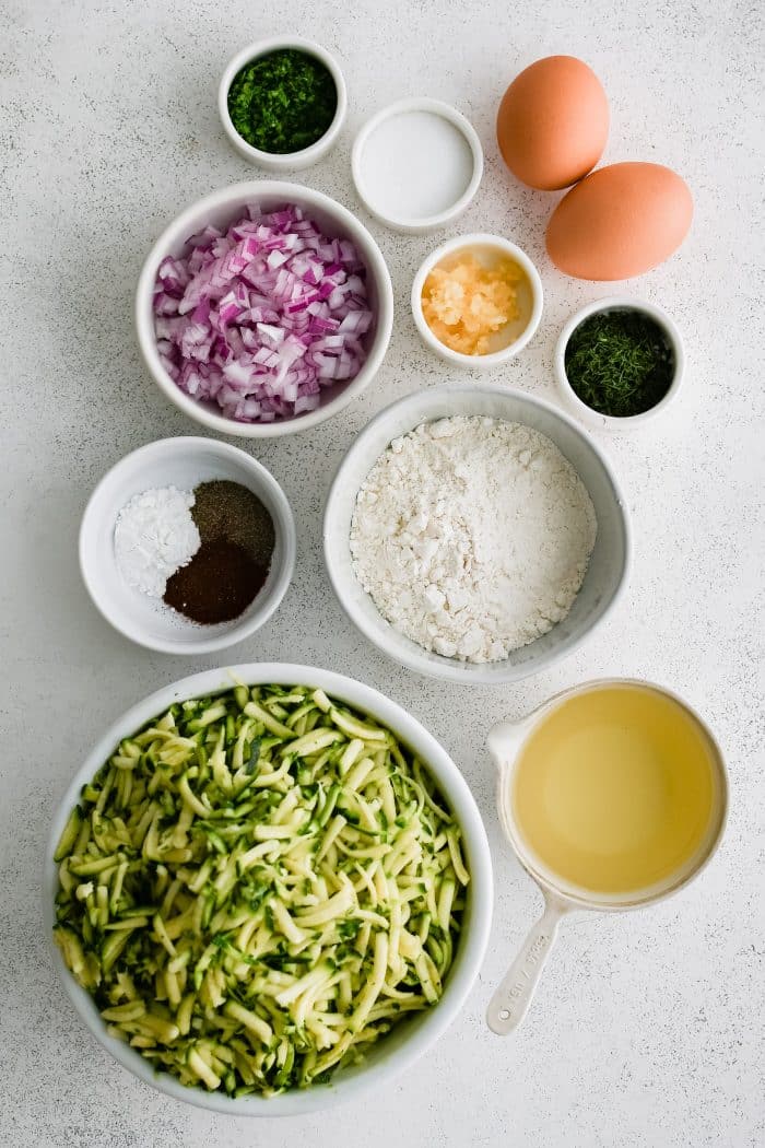 All of the ingredients needed to make super crispy zucchini fritters in individual measuring cups and ramekins.