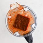Bowl of a high speed blender filled with blended leftover solids from strained chile colorado sauce and chicken broth.