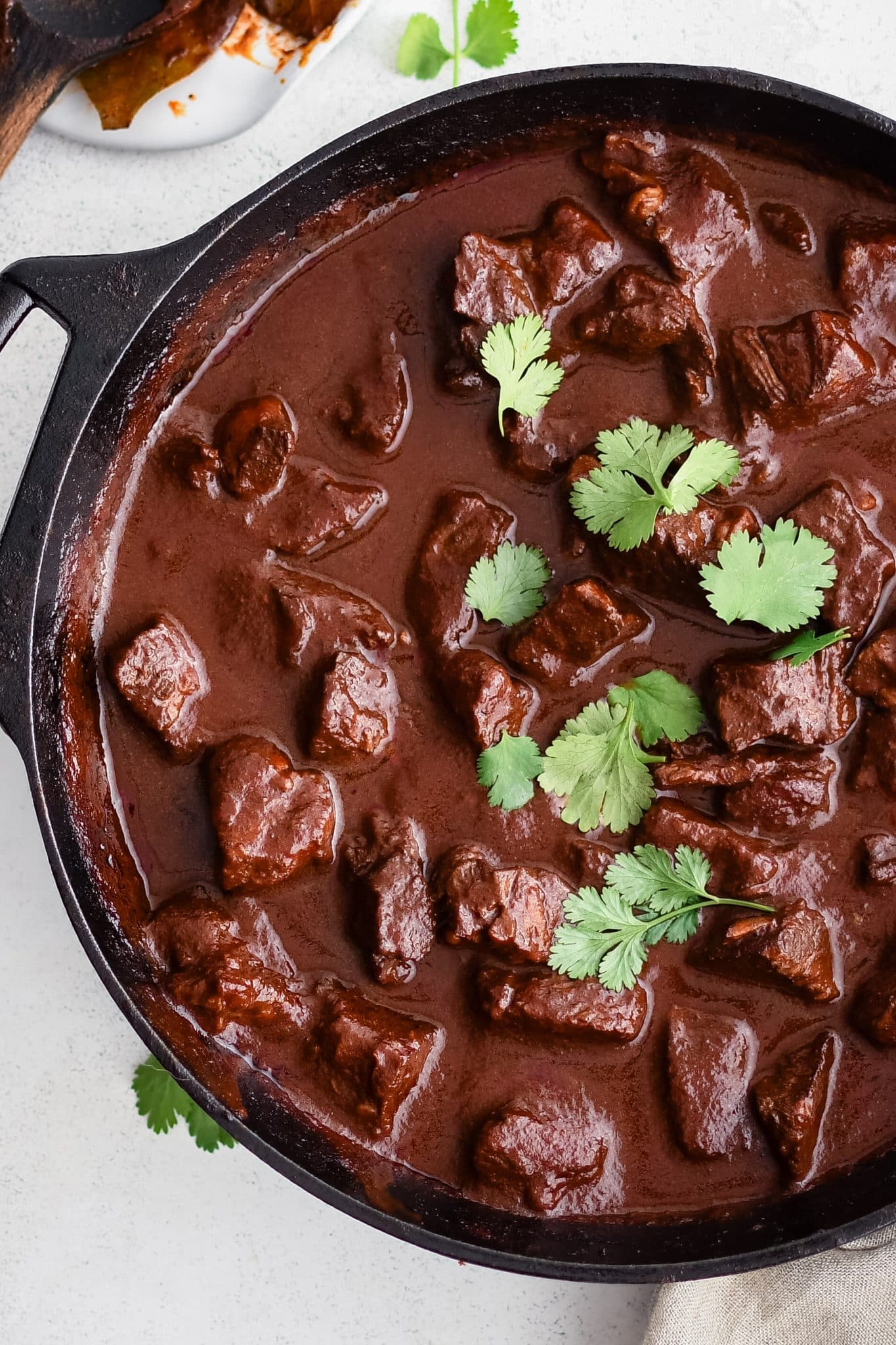 Homemade chile colorado with chunks of beef in a large cast iron pot and garnished with fresh cilantro.