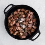Seared chunks of beef chuck seasoned with salt and black pepper in a large cast iron pan.