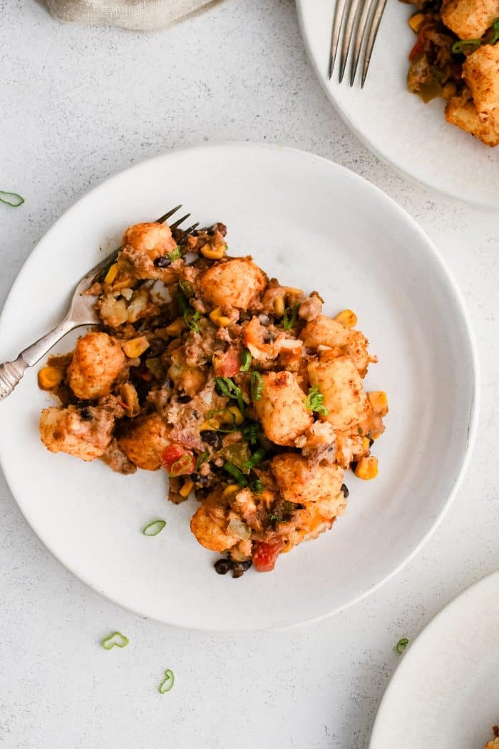 A white serving plate with a generous serving of baked cowboy casserole including several crispy baked tater tots.