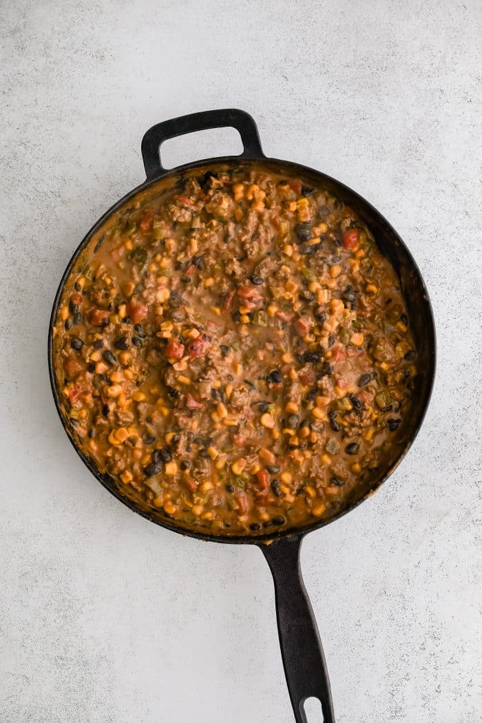 Cheesy, meaty filling for cowboy casserole in a large cast iron skillet.