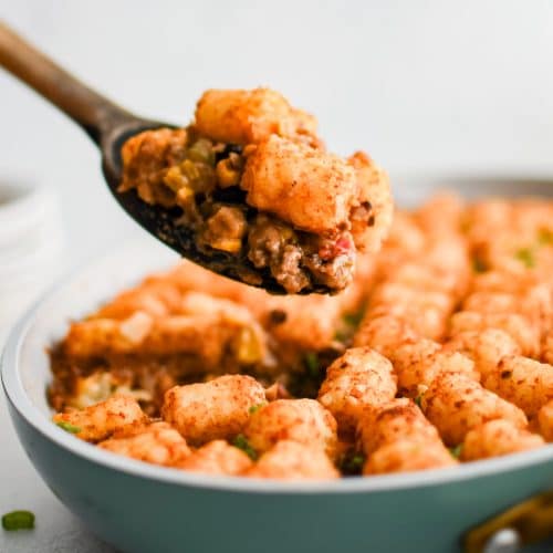 Wooden serving spoon filled with a generous serving of cowboy casserole including several crispy tater tots.