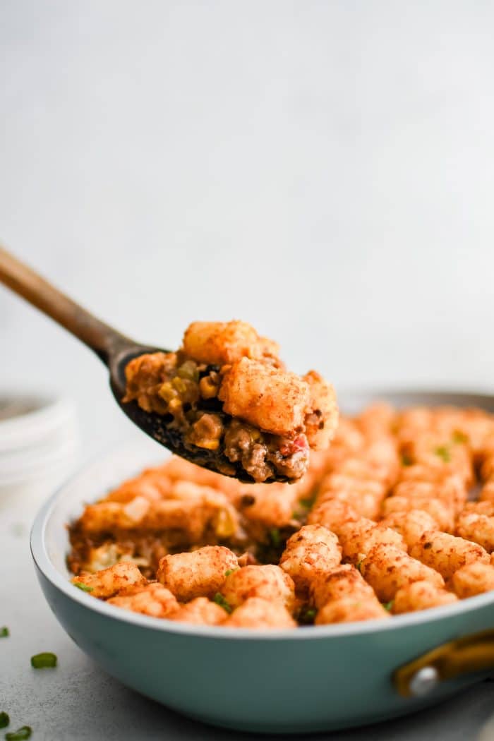 Wooden serving spoon filled with a generous serving of cowboy casserole including several crispy tater tots.