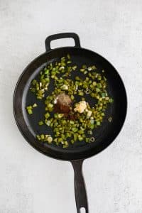 Minced garlic, paprika, salt, and black pepper added to a large cast iron skillet filled with softened green onions and green bell pepper.