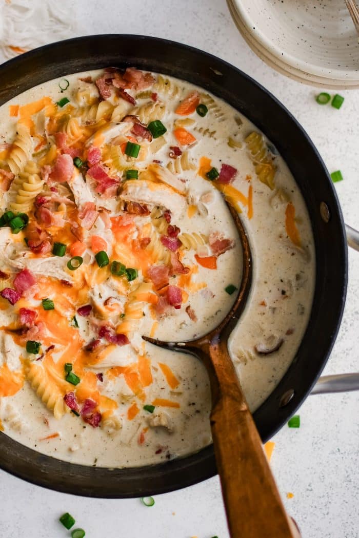 Large soup pot filled with super creamy crack chicken soup made with rotini pasta, shredded chicken, and bacon in a cream based broth, and topped with shredded cheddar cheese, chopped green onions, and even more crispy cooked bacon bits.