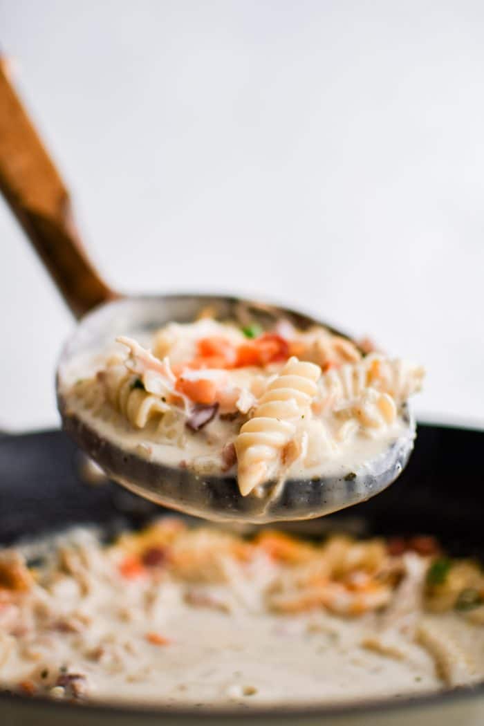 Soup ladle filled with creamy crack chicken soup made with shredded chicken, cooked rotini pasta, and bacon in a creamy broth.