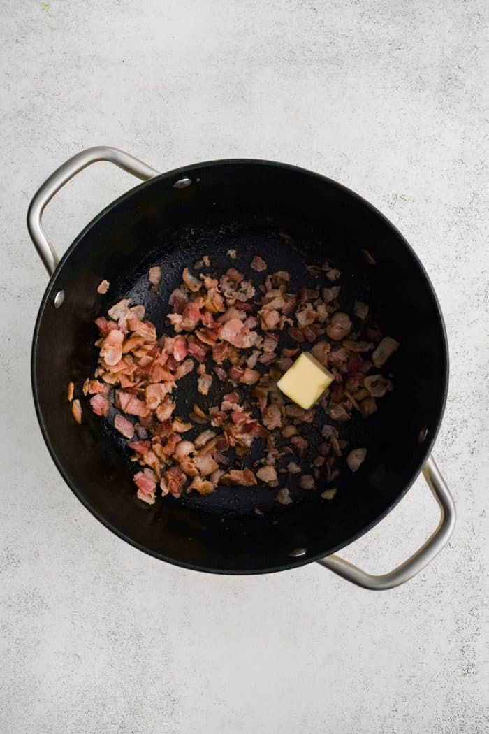 Large soup pot filled with crispy cooked bacon bits and a pat of melting butter.