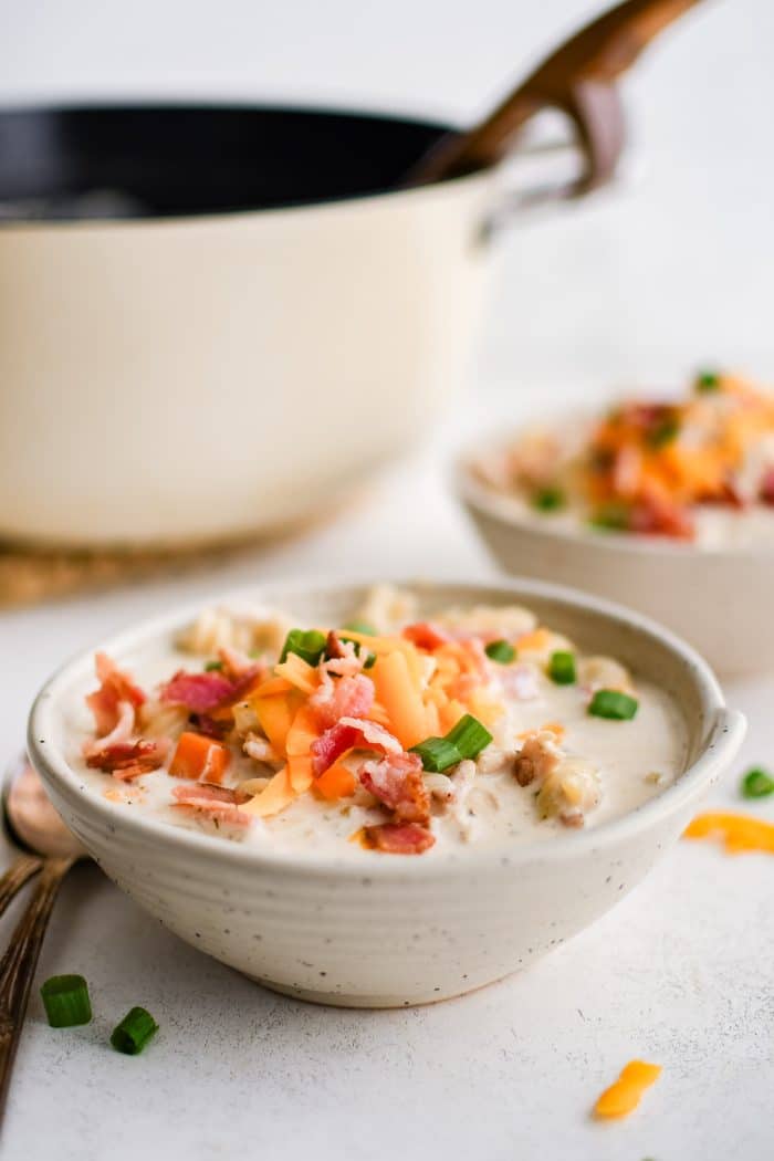 Bowl filled with super creamy crack chicken soup filled with rotini pasta, shredded chicken, bacon, and topped with shredded cheddar cheese, chopped green onions, and even more crispy cooked bacon bits.