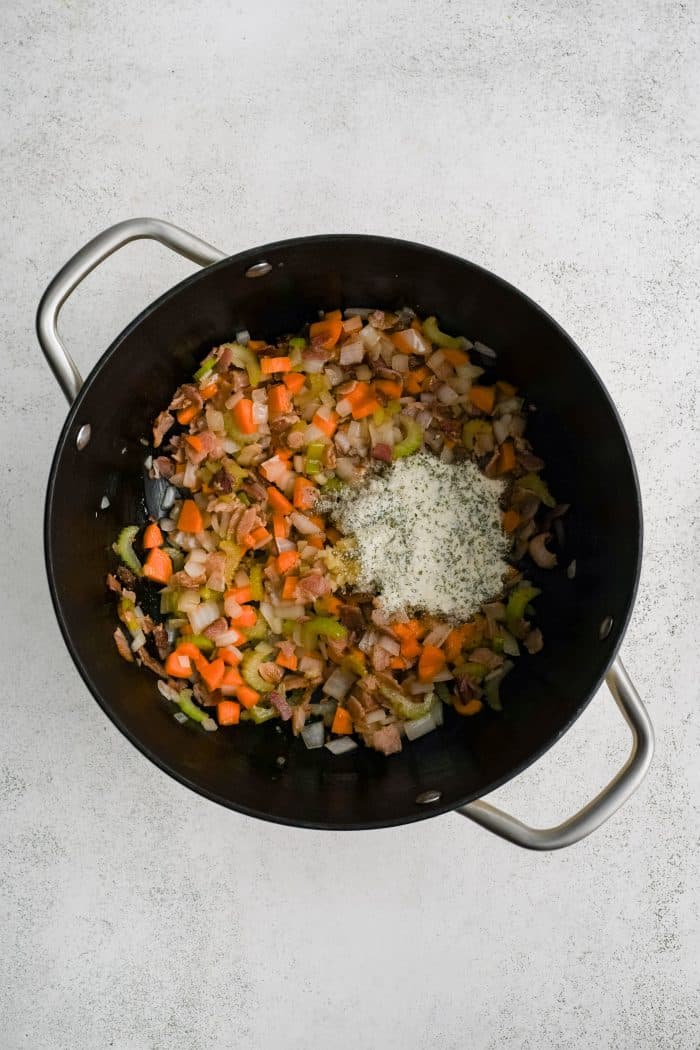 Dry ranch seasoning and garlic added to a large pot filled with carrots, onions, and celery sautéeing in butter.