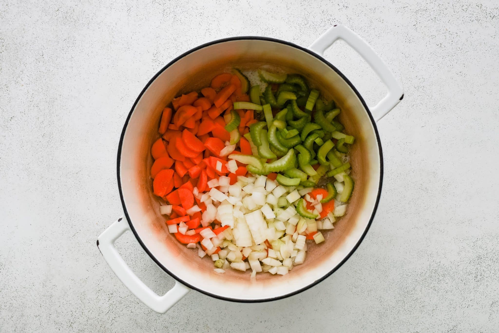 Chopped carrots, celery, and onions in a large white Dutch oven. 