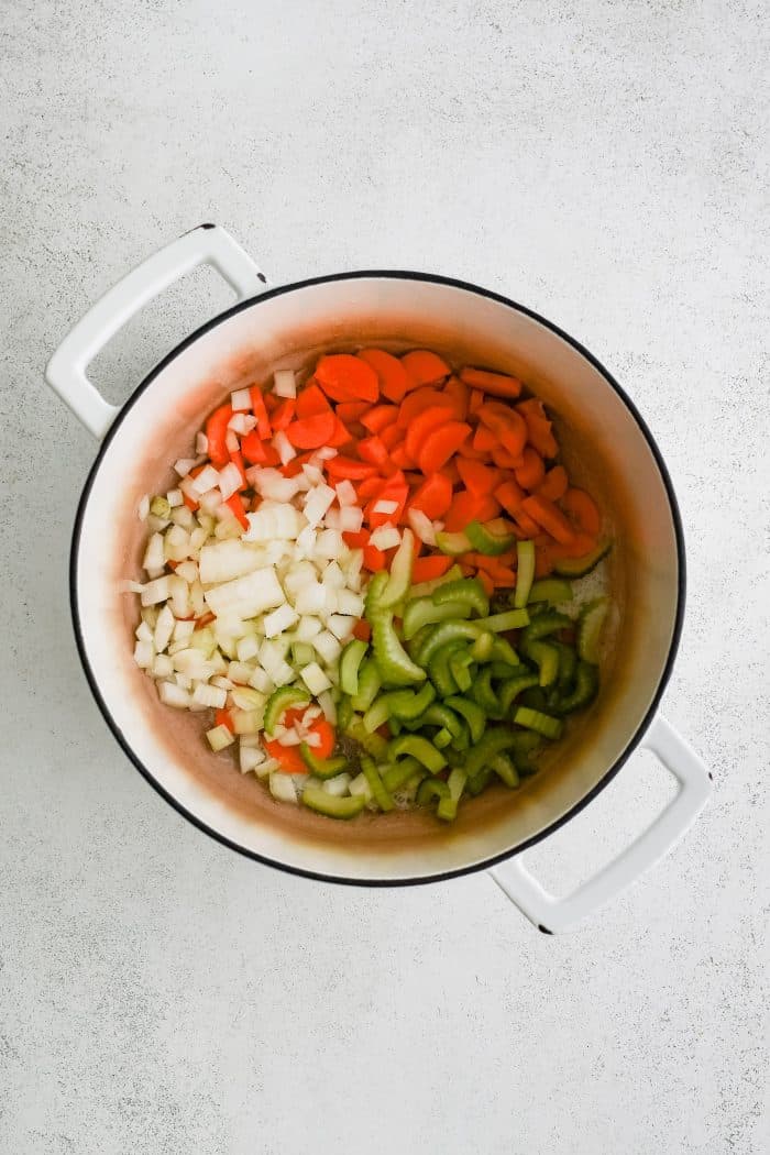 Diced onions, celery, and carrots in a large white enameled Dutch oven.