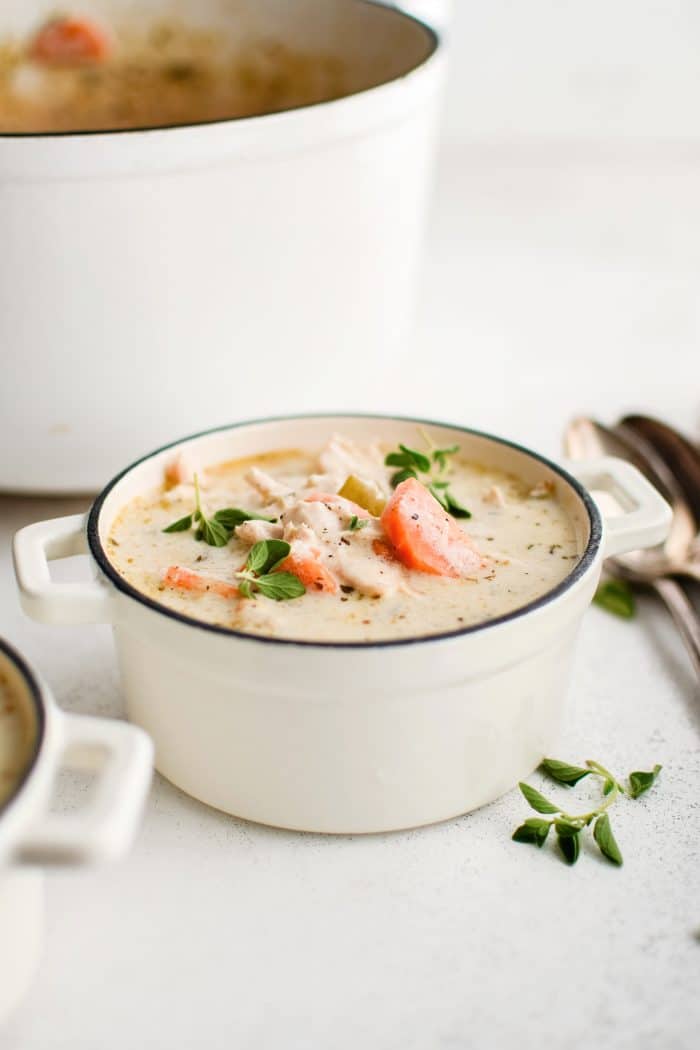 Small white soup bowl filled with creamy chicken soup garnished with fresh parsley and oregano.