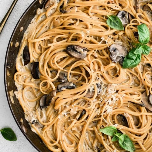 Creamy mushroom linguine pasta in a large cast iron skillet garnished with additional grated parmesan cheese and fresh basil leaves.