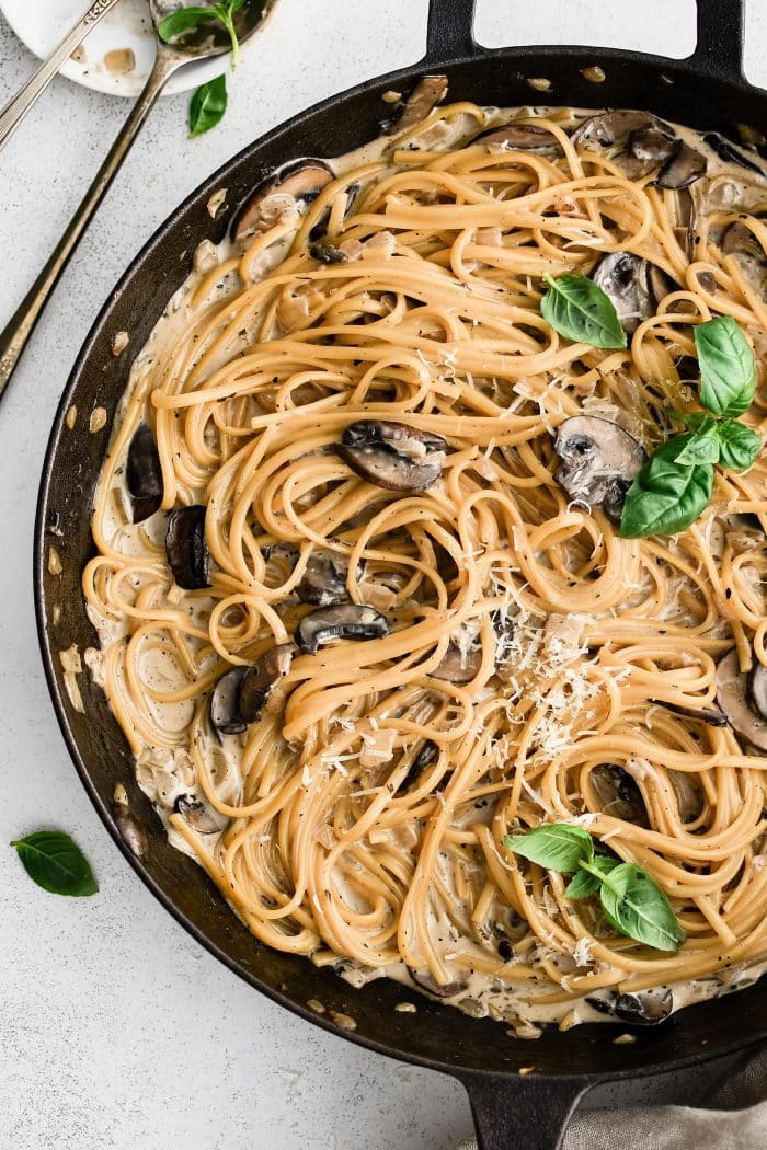 Creamy mushroom linguine pasta in a large cast iron skillet garnished with additional grated parmesan cheese and fresh basil leaves.