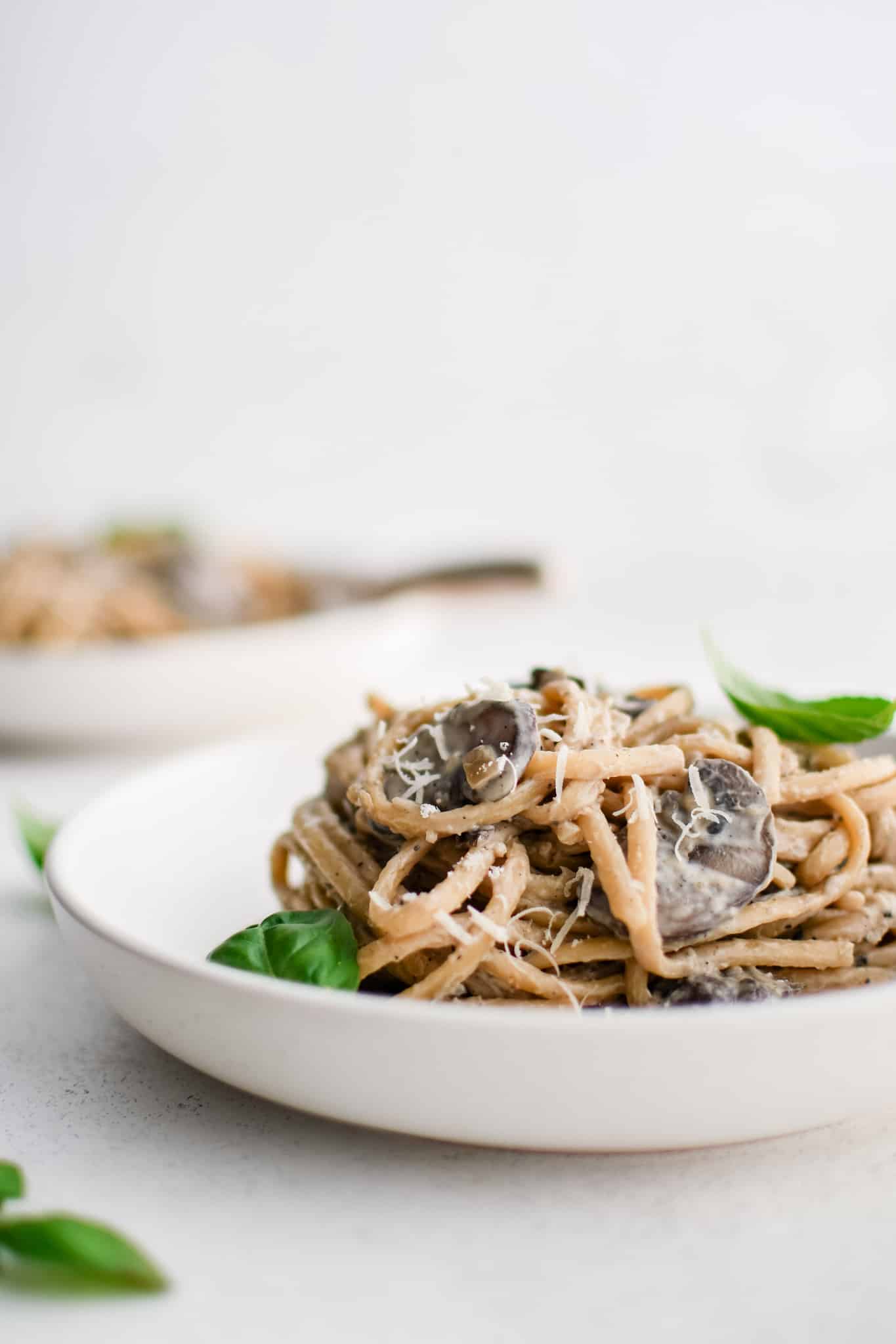 Shallow pasta bowl filled with creamy mushroom pasta garnished with grated Parmesan cheese and fresh basil leaves.