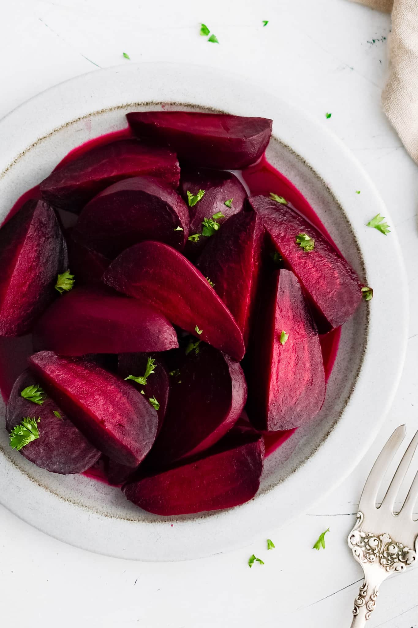 White plate filled with cooked, peeled, and sliced red beets garnished with chopped parsley.