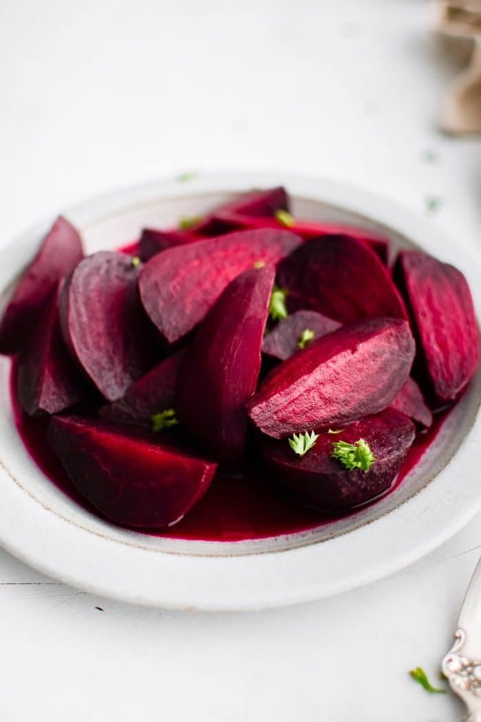 White plate filled with cooked, peeled, and sliced red beets garnished with chopped parsley.