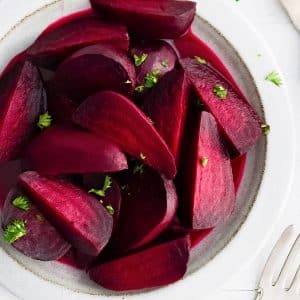 White plate filled with cooked, peeled, and sliced red beets garnished with chopped parsley.