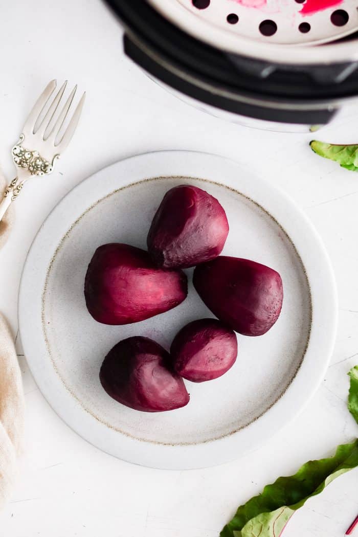 Five medium-sized cooked and peeled red beets on a white plate.