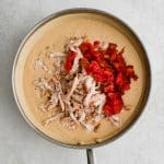 Cooked and shredded chicken and drained Ro-tel tomatoes added to a large skillet filled with homemade creamy cheese sauce.