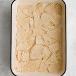 Large casserole dish with a bottom layer of torn corn tortilla pieces.