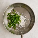 Large skillet filled with hot oil and diced green bell pepper and white onion.