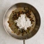 Large skillet filled with sautéed diced bell pepper and onions coated in chili powder, salt, and black pepper, and sprinkled with all purpose flour.