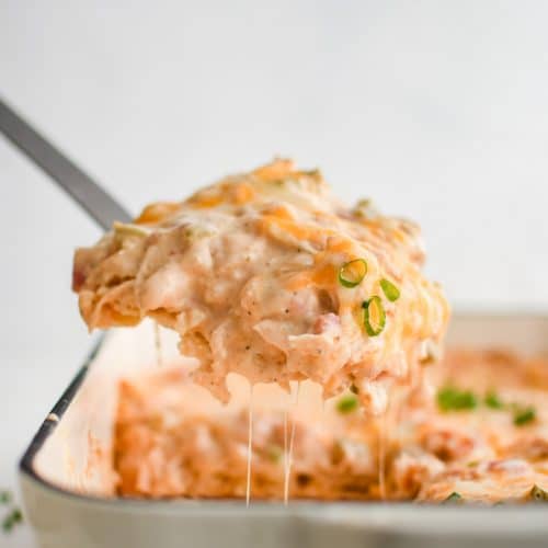 Large metal spatula scooping a large serving of hot and cheese King Ranch chicken casserole from a large white baking dish.