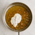 Chicken broth and sour cream added to a large skillet filled with sautéed diced bell pepper and onions coated in chili powder, salt, black pepper, and all purpose flour.