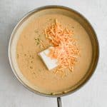 Shredded Colby Jack cheese and cream cheese add to a skillet filled with thickened sour cream and veggie sauce.