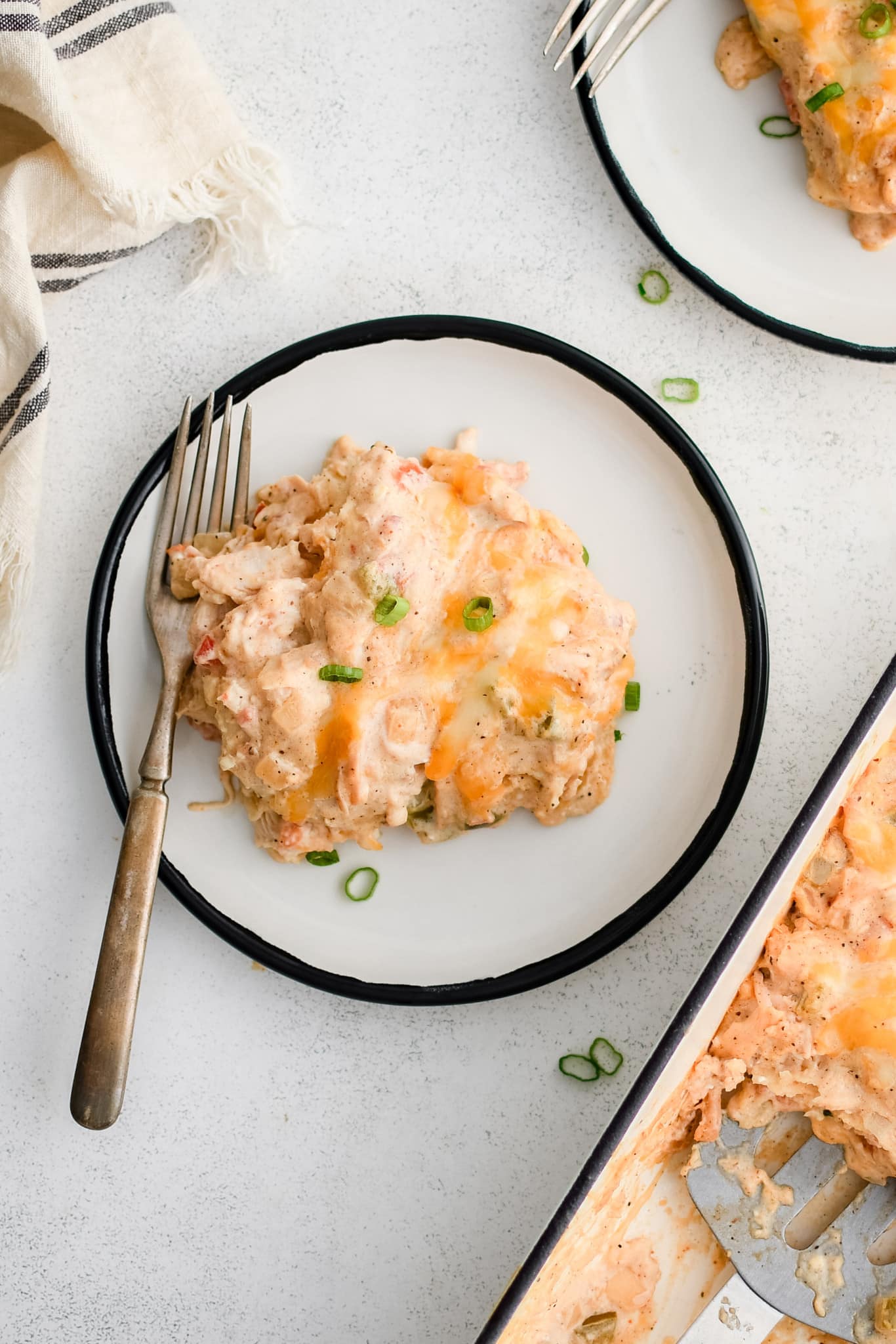 Serving of King Ranch chicken casserole on a white serving plate with a fork and garnished with sliced green onions.