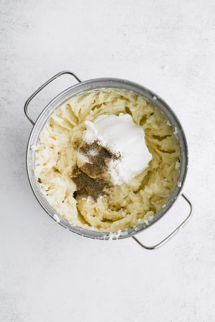 Sour cream and black pepper added to a large pot filled with mashed potatoes.