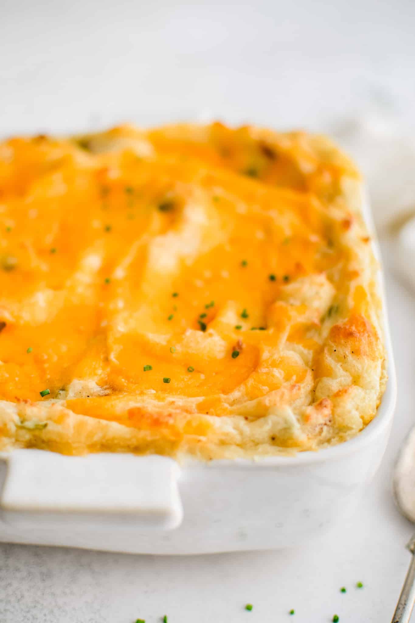 A white 9x9-inch casserole dish filled with loaded mashed potatoes and baked with a layer of gooey melted cheddar cheese.