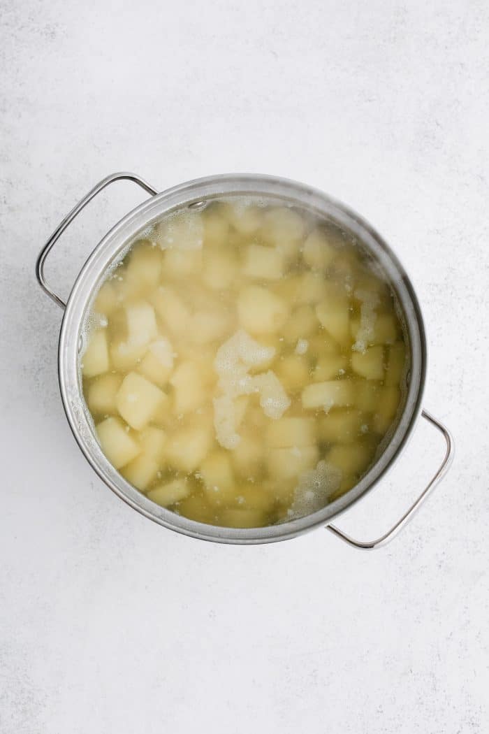 Large pot filled with peeled and chopped potatoes cooking in boiling water.