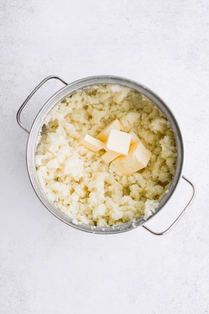 Large pot filled with melting half sticks of butter on top of mashed potatoes.