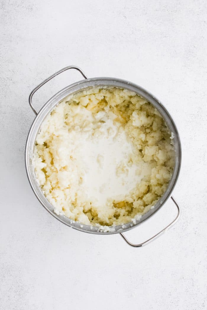 Milk added to a large pot filled with buttery mashed potatoes.