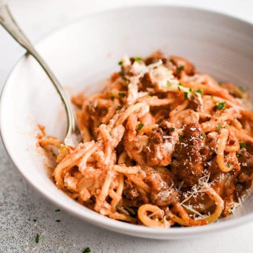 A white pasta dish filled with a serving of million dollar spaghetti casserole a garnished with fresh minced parsley and grated parmesan cheese.