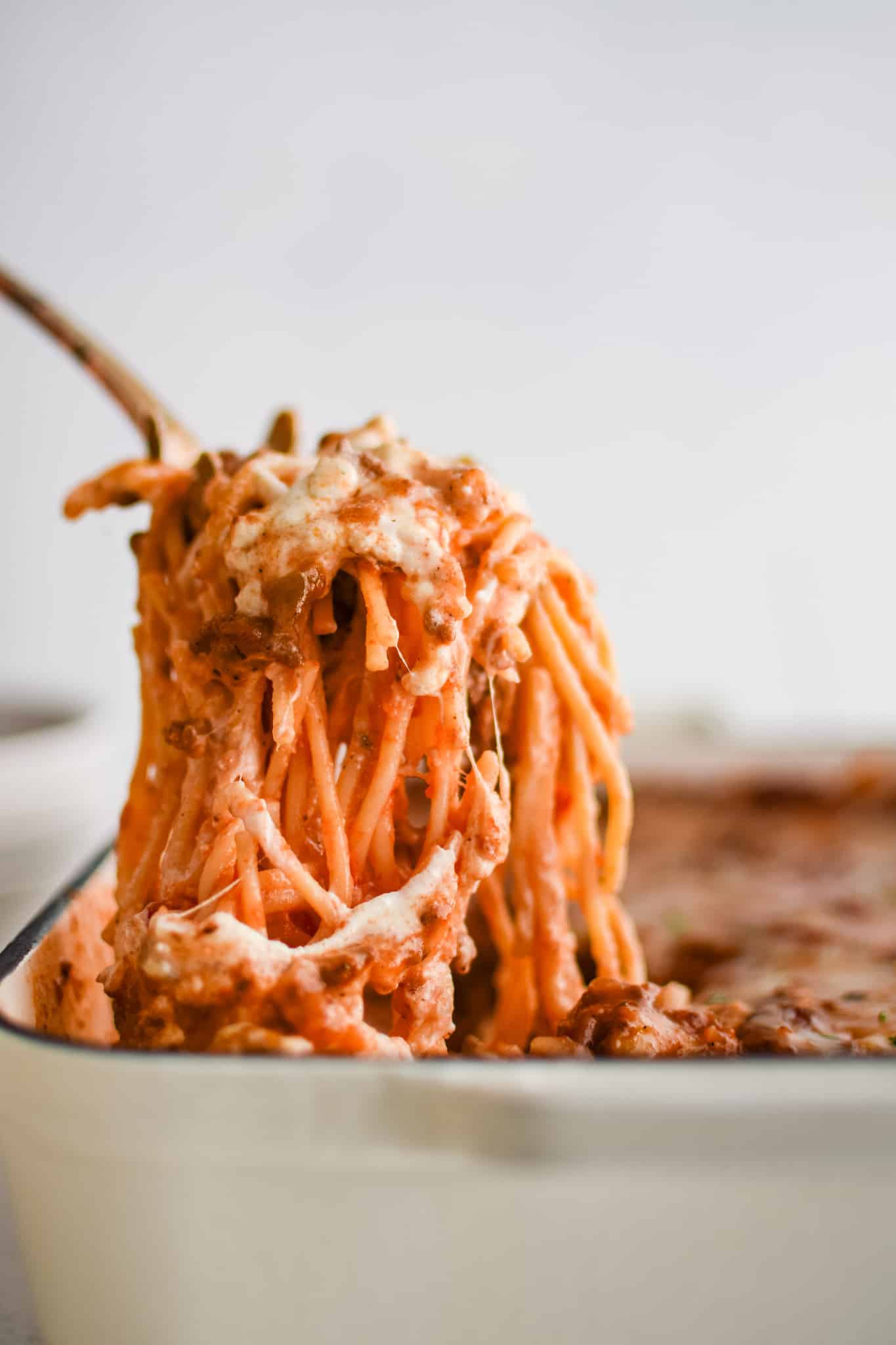A serving of cheesy million dollar casserole being lifted from a large casserole dish.