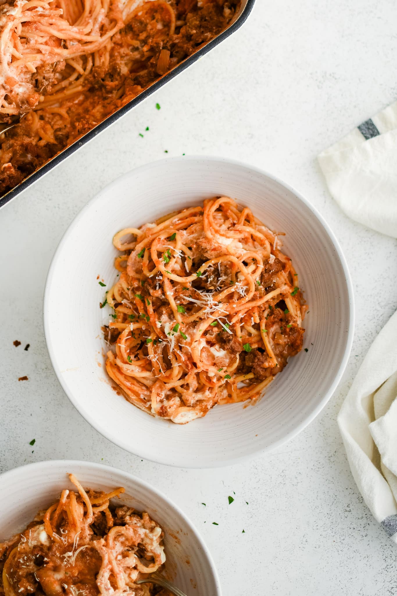 A white pasta dish filled with a serving of million dollar spaghetti casserole a garnished with fresh minced parsley and grated parmesan cheese.