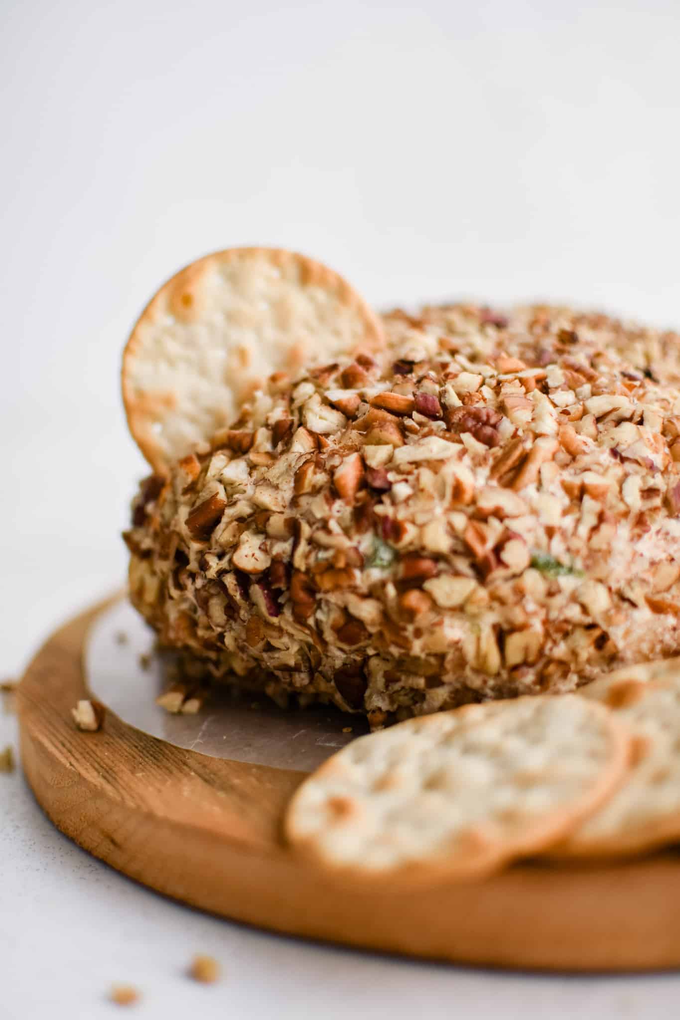 Pineapple cheese ball in the shape of a disc and coated in pecans on a small wood cutting board with a single cracker stuck in the center.