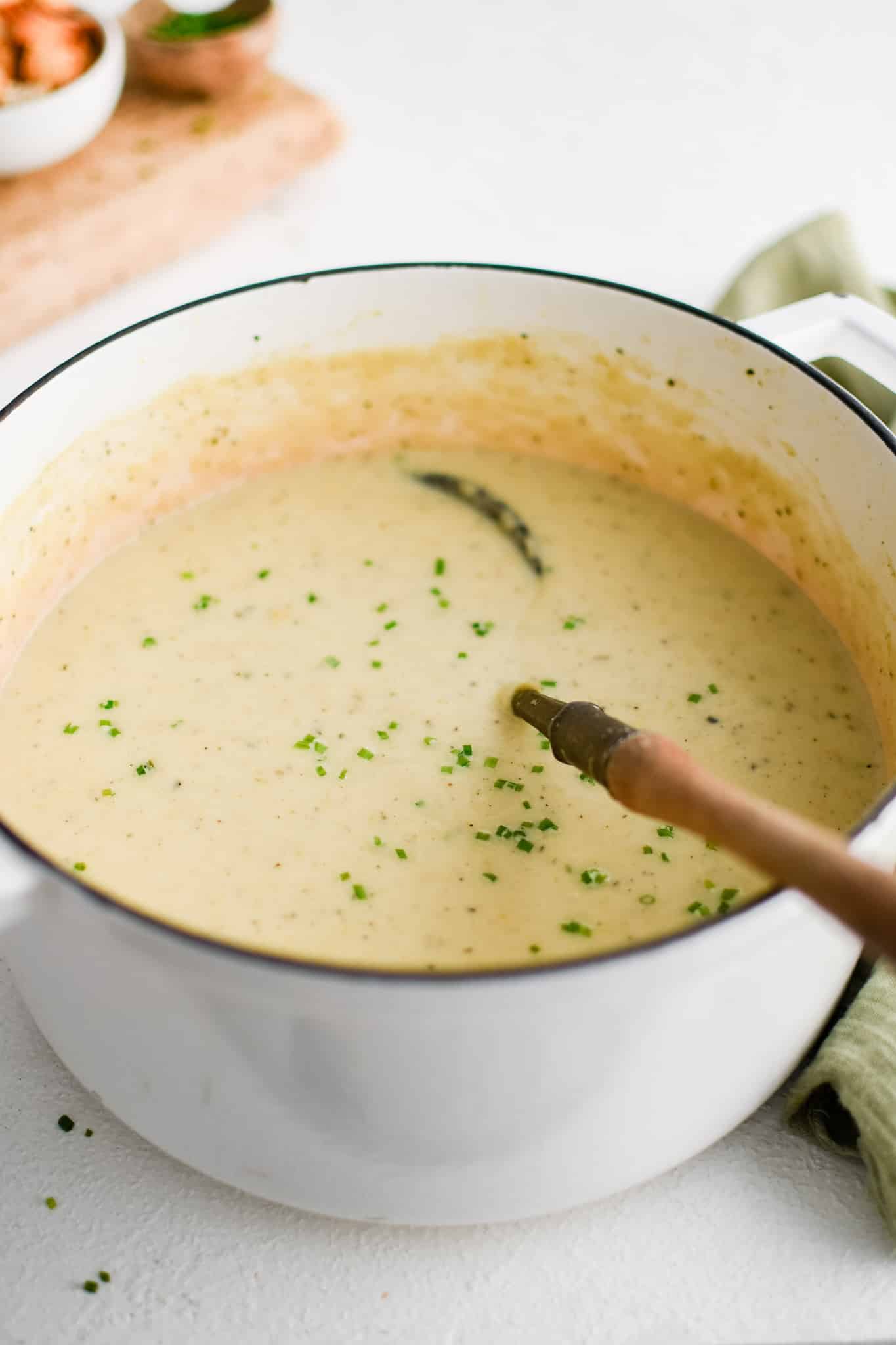 Large white pot filled with creamy potato and leek soup garnished with freshly chopped parsley.