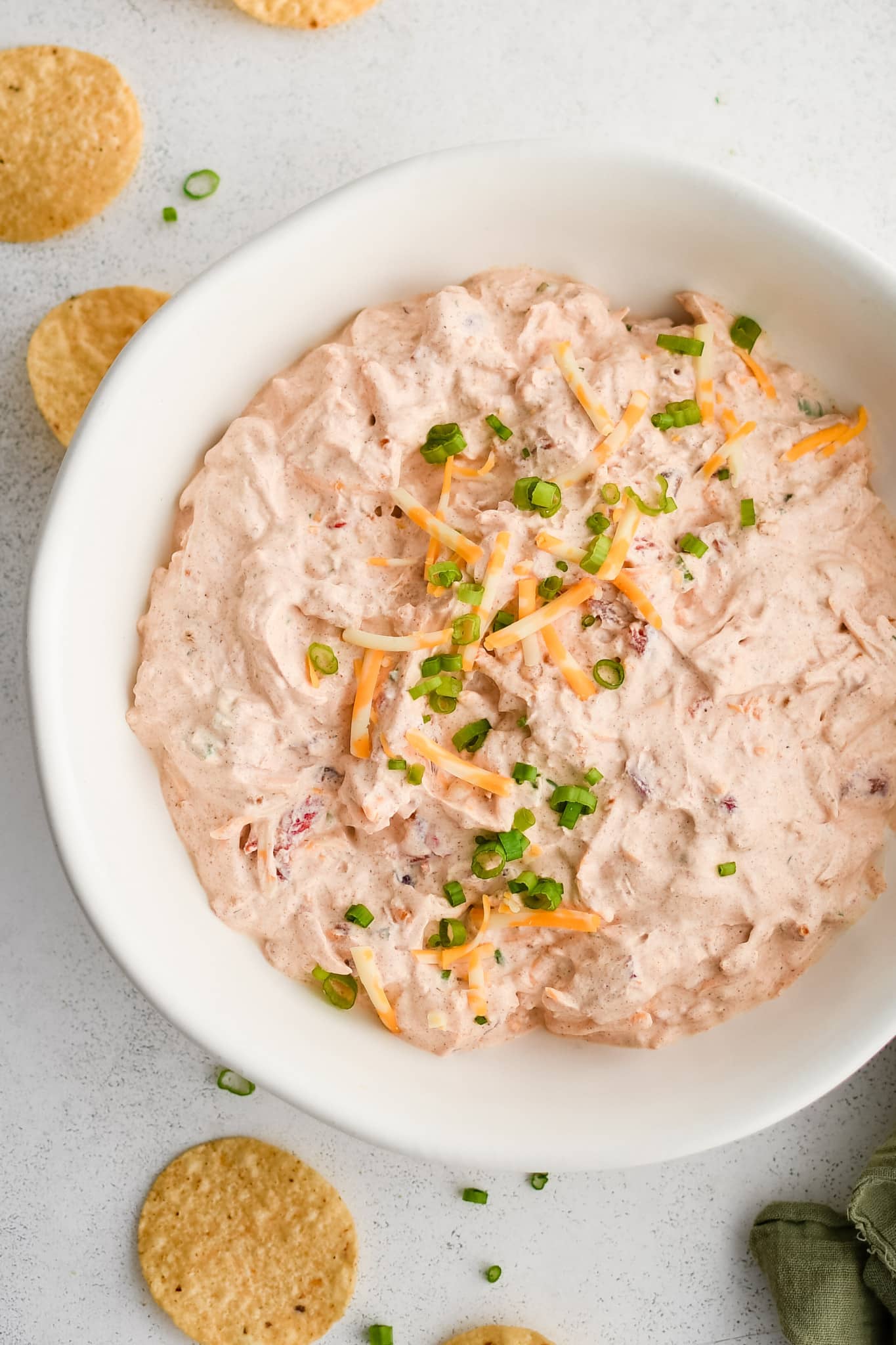 Boat dip made with shredded cheddar cheese, green onions, sour cream, drained rotel tomatoes, taco seasoning, and ranch seasoning in a large white serving bowl and garnished with additional shredded cheese and green onions.