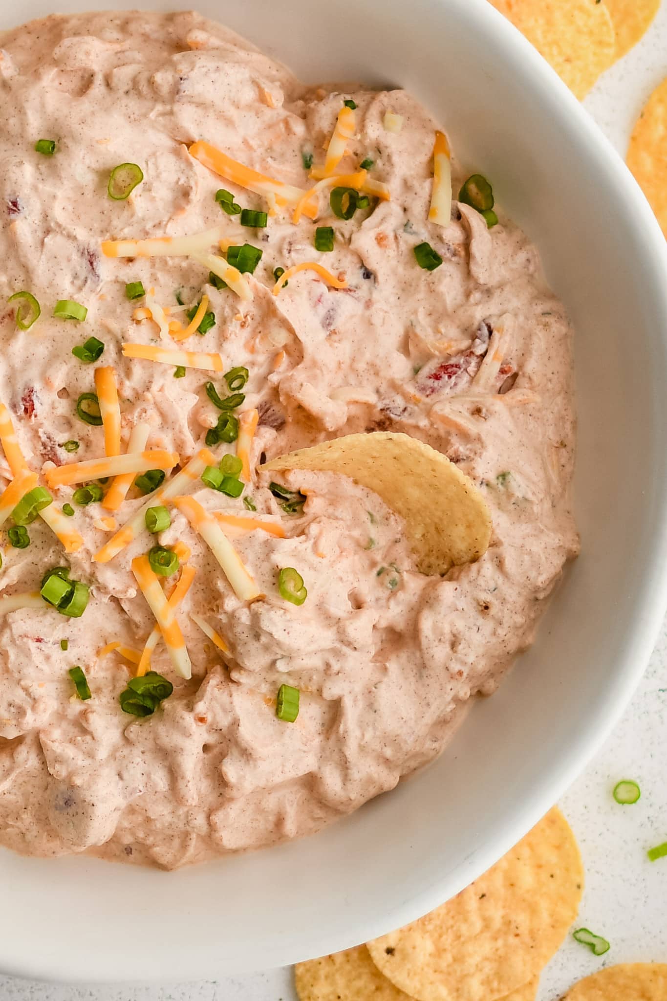 Round tortilla chip stuck halfway in a bowl filled with boat dip made with shredded cheddar cheese, green onions, sour cream, drained rotel tomatoes, taco seasoning, and ranch seasoning.
